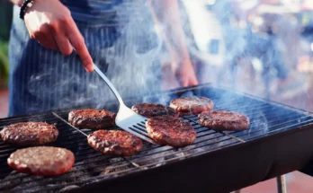 A person grilling burgers on a smoky backyard barbecue | Source: Shutterstock
