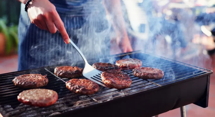 A person grilling burgers on a smoky backyard barbecue | Source: Shutterstock