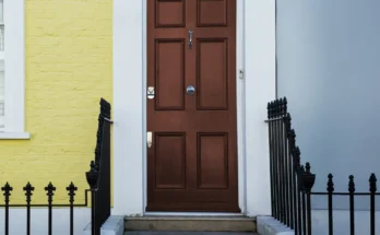 A brown front door framed by a yellow brick wall and soft blue siding | Source: Freepik