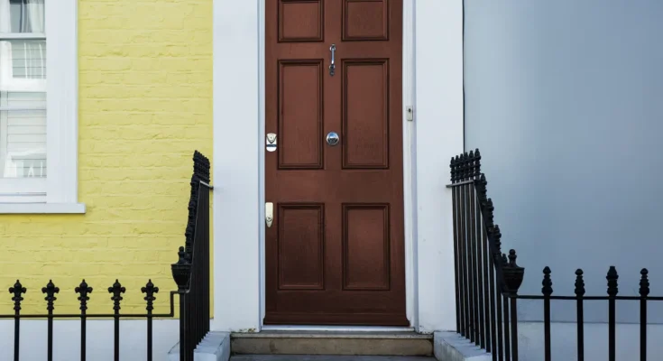 A brown front door framed by a yellow brick wall and soft blue siding | Source: Freepik