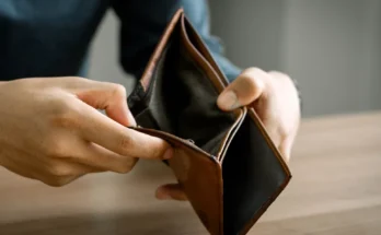 A person holding an open, empty brown wallet over a wooden table | Source: Shutterstock