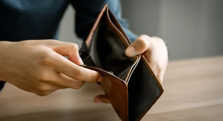 A person holding an open, empty brown wallet over a wooden table | Source: Shutterstock