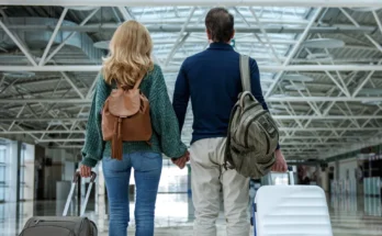 A couple standing hand in hand in an airport, each holding a suitcase | Source: Shutterstock