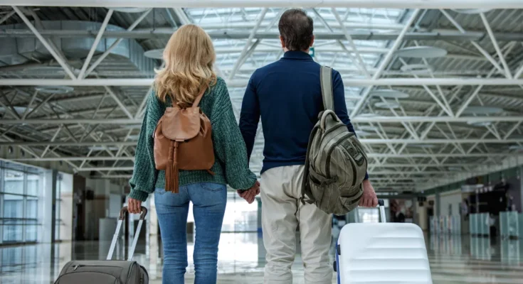 A couple standing hand in hand in an airport, each holding a suitcase | Source: Shutterstock