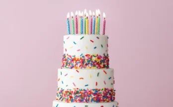 A three-tiered birthday cake with rainbow sprinkles and lit candles | Source: Shutterstock