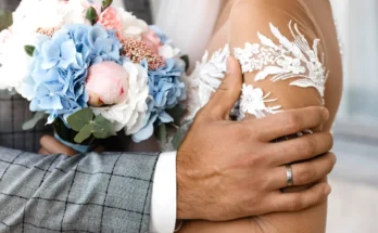 A groom gently holds his bride, their hands wrapped around a bouquet of pastel flowers | Source: Freepik